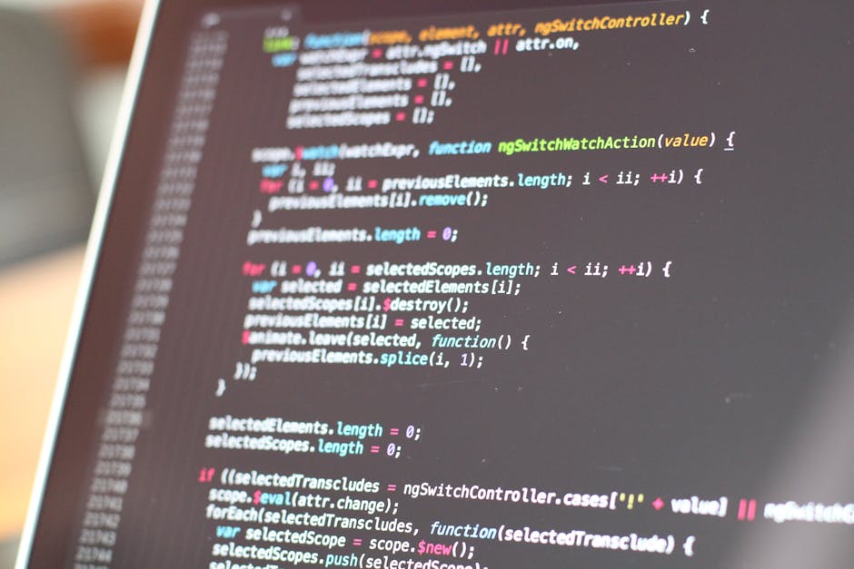 A close-up view of a computer screen displaying colorful lines of programming code, including text in shades of green, blue, pink, and white on a dark background. The screen appears slightly tilted, w